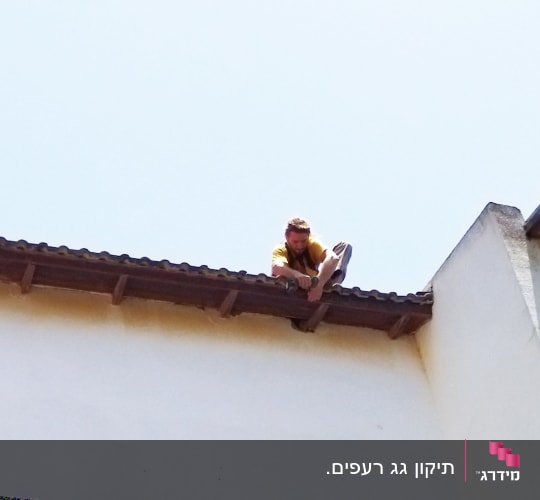אדם יושב על גג רעפים עם כלי עבודה ביד